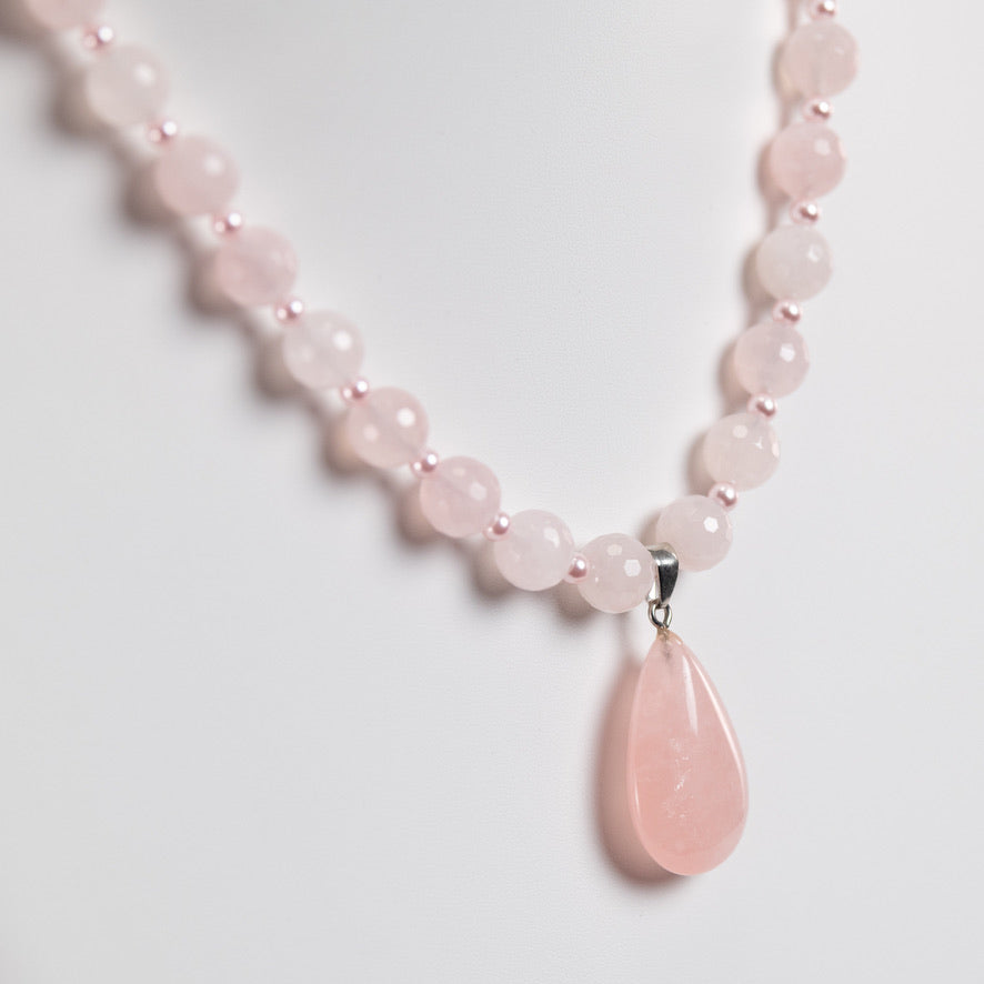 Necklace with pink beads and a teardrop pendant on a light gray background